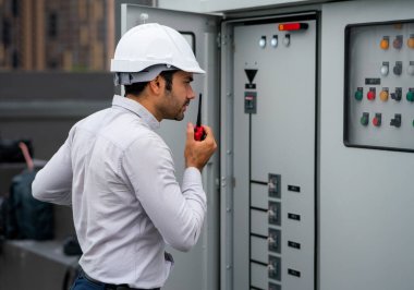 Caucasian engineer man or technician using walkie talkie to contact his coworker and ask for support about electrical control panel in construction site.