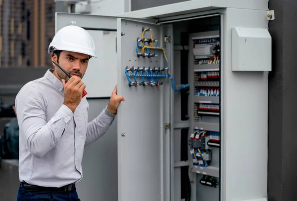 Professional engineer man open lid of electrical control panel and use walkie talkie to contact and ask for support from his coworker at workplace of construction site.