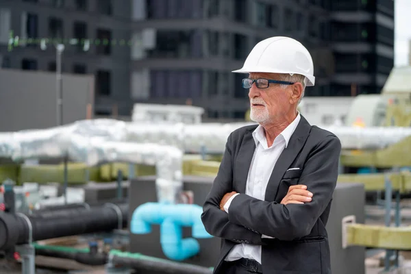 Senior engineer man stand with arms crossed and look to his right side also stand on rooftop of construction site.