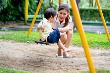 Asian mother have fun with her little boy to play together with swing in garden during day time.