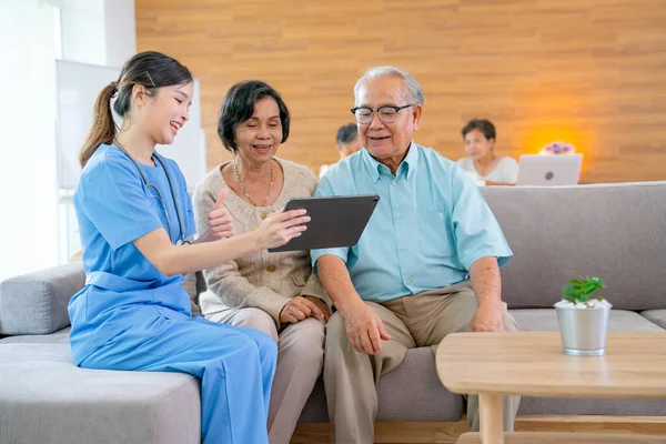 Beautiful Asian nurse or doctor use tablet to consult and give assistant to couple senior man and woman in living room of clinic or hospital in senior healthcare center