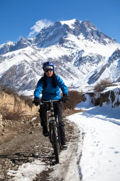 Girl on bike rides in the snow in the high mountains of the HimalayasAnnapurna track Himalayas — Stock Photo, Image