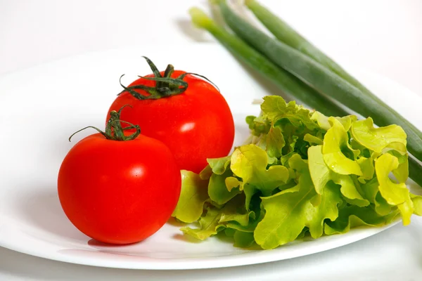 Pomodori e cipolla verde su un piatto bianco — Foto Stock
