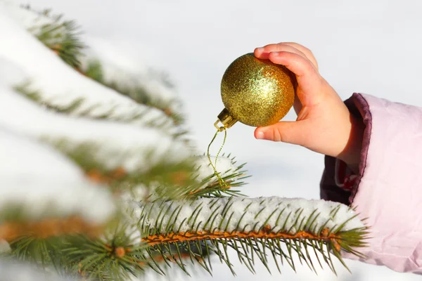 Child hangs the ball on the Christmas tree in winter — Stock Photo, Image