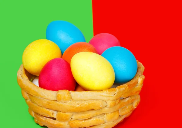 Cesta assada com ovos coloridos de Páscoa no fundo verde e vermelho — Fotografia de Stock