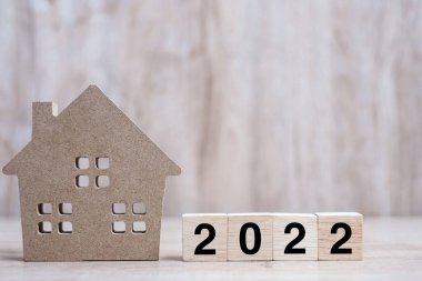 2022 Mutlu Yıllar, masa başı ahşap arka planda ev modeliyle. Bankacılık, gayrimenkul, yatırım, finans, tasarruf ve yeni yıl kararı kavramları