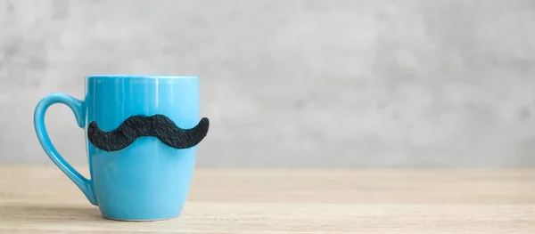 Blue coffee cup or tea mug with Black mustache decor on table. Blank copy space for text. Blue November, Happy Father day and International men day concept