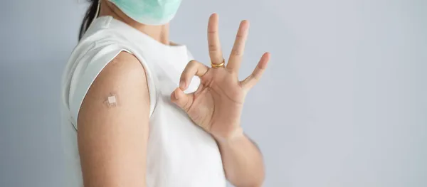 woman showing OK sign with bandage after receiving covid 19 vaccine. Vaccination, herd immunity, side effect, booster, vaccine passport and Coronavirus pandemic