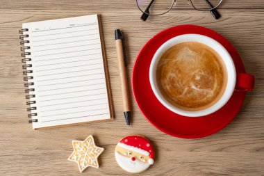 Boş defter, sade kahve fincanı, Noel kurabiyeleri ve tahta masa üzerindeki kalem, üst manzara ve fotokopi alanı. Xmas, Mutlu Yıllar, Hedefler, Kararlılık, Yapılacaklar listesi, Strateji ve Planlama konsepti