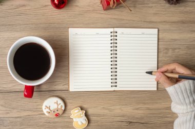 Not defterine siyah kahve fincanı ve masada Noel kurabiyesi olan bir kadın el yazısı. Xmas, Mutlu Yıllar, Hedefler, Kararlılık, Yapılacaklar listesi, Strateji ve Planlama konsepti