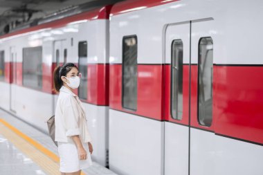 Tren beklerken koruyucu yüz maskesi takan kadın Coronavirus bükülmesini önlüyor. Toplu taşıma. Sosyal uzaklık, covid-19 salgını altında yeni normal ve güvenlik