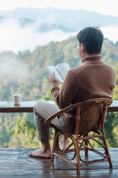 Ung Man Läser Bok Nära Fönstret Och Tittar Bergsutsikt Landsbygden — Stockfoto