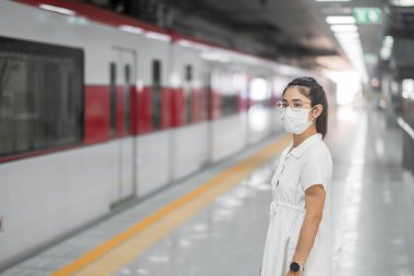 Tren beklerken koruyucu yüz maskesi takan kadın Coronavirus bükülmesini önlüyor. Toplu taşıma. Sosyal uzaklık, covid-19 salgını altında yeni normal ve güvenlik