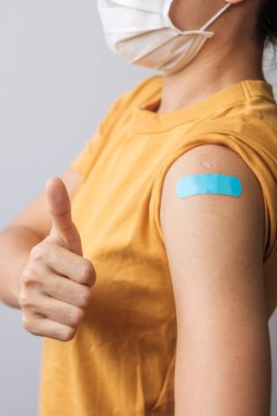 woman showing Thumb sign with bandage after receiving covid 19 vaccine. Vaccination, herd immunity, side effect, booster dose, vaccine passport and Coronavirus pandemic clipart
