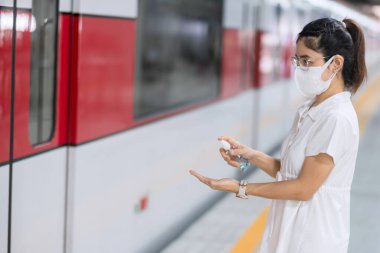 Trende ya da toplu taşımada alkollü jel dezenfektanı ya da Coronavirus hastalığı enfeksiyonunu koruyan bir kadın. COVID-19 kavramları altında kişisel hijyen, güvenlik ve seyahat ulaşımı