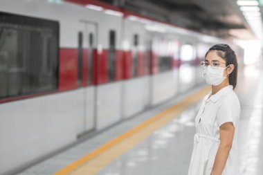 Tren beklerken koruyucu yüz maskesi takan kadın Coronavirus bükülmesini önlüyor. Toplu taşıma. Sosyal uzaklık, covid-19 salgını altında yeni normal ve güvenlik
