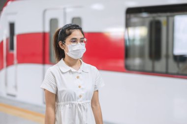 Tren beklerken koruyucu yüz maskesi takan kadın Coronavirus bükülmesini önlüyor. Toplu taşıma. Sosyal uzaklık, covid-19 salgını altında yeni normal ve güvenlik