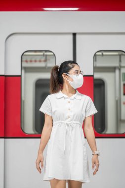 Tren beklerken koruyucu maske takan mutlu bir kadın koronavirüs bükülmesini önlüyor. Toplu taşıma. Sosyal uzaklık, covid-19 salgını altında yeni normal ve güvenlik