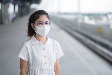 Korunaklı yüz maskesi takan kadın koronavirüs ve 2,5 numaralı tren beklerken başbakan kirliliği. Toplu taşıma. Covid-19 salgını ve toz altında güvenlik