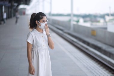 Korunaklı yüz maskesi takan kadın koronavirüs ve 2,5 numaralı tren beklerken başbakan kirliliği. Toplu taşıma. Covid-19 salgını ve toz altında güvenlik