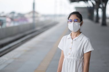 Korunaklı yüz maskesi takan kadın koronavirüs ve 2,5 numaralı tren beklerken başbakan kirliliği. Toplu taşıma. Covid-19 salgını ve toz altında güvenlik