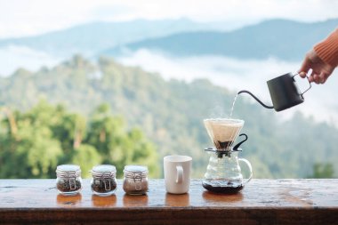 Hand pouring Hot water during brewing arabica coffee by Vintage coffee drip equipment on wooden table in the morning with mountain and nature background