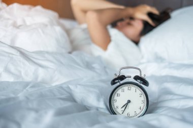 Asyalı bir kadın sabahın köründe alarmlı saatle yatakta yatıyor. Genç bir kadın yatak odasında uyuyor. Huzursuz, uykusuz, uykusuz, endişeli ve stresli kavramlar