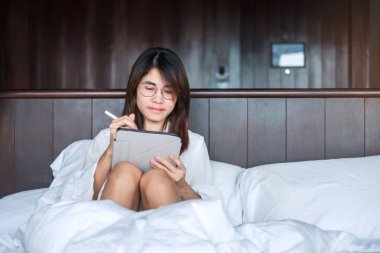 Sosyal medya için tablet kullanan mutlu bir kadın, evdeki yatakta bilgisayar ekranında film izleyen genç bir kadın. teknoloji, ağ, çevrimiçi alışveriş, e ticaret, yaşam tarzı ve dijital iletişim kavramı