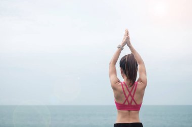 Yoga yapan ve kaslarını esneten genç bir kadın. Okyanus manzarasına karşı sağlıklı kız meditasyonu. Zindelik, zindelik, zindelik, egzersiz ve iş hayatı dengesi kavramları