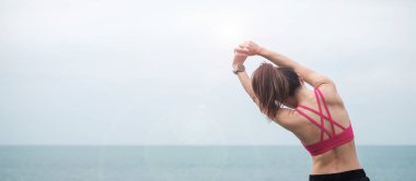 Spor kıyafetli genç bir kadın, vücudu okyanus manzarasına karşı esnetiyor, sabahları sağlıklı kadın egzersizi yapıyor. Spor, sağlık ve iş hayatı dengesi kavramları