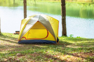 Ormanın altında kamp, göl kenarında sarı çadır. Açık hava seyahati, gezi ve tatil konsepti