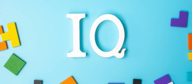 Renkli ahşap yapboz parçalı IQ metni, mavi arka planda geometrik şekil bloğu. Zeka niceliği ve mantık düşüncesi kavramı