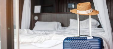 Kapı açıldıktan sonra modern otel odasında şapkalı mavi bavul. Seyahat, hizmet, yolculuk, seyahat, yaz tatili ve tatil kavramları