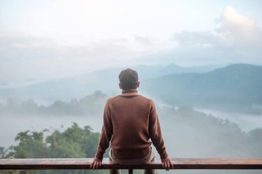 happy tourist man relaxing and looking mountain view at countryside home or homestay in the morning. Vacation, blogger, SoloTravel, journey, trip and relaxing concept