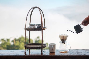 Hand pouring Hot water during brewing arabica coffee by Vintage coffee drip equipment on wooden table in the morning with mountain and nature background