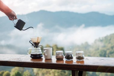 Hand pouring Hot water during brewing arabica coffee by Vintage coffee drip equipment on wooden table in the morning with mountain and nature background