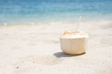 Taze hindistan cevizi suyu ve tropik plaj arka planına karşı beyaz kumda saman. Yaz, dinlenme ve tatil kavramları
