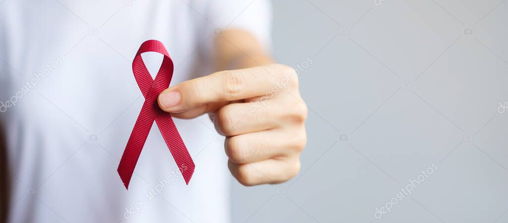 hand holding Burgundy Red Ribbon for March multiple myeloma Cancer and December World Aids Day Awareness month. Healthcare and world cancer day concept