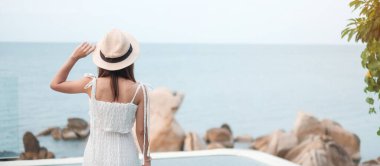 Beyaz elbiseli ve şapkalı mutlu gezgin kadın güzel deniz manzarasının keyfini çıkar, havuzda duran genç kadın. Özgürlük, dinlenme, tatil ve yaz seyahati konsepti