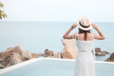 Beyaz elbiseli ve şapkalı mutlu gezgin kadın güzel deniz manzarasının keyfini çıkar, havuzda duran genç kadın. Özgürlük, dinlenme, tatil ve yaz seyahati konsepti