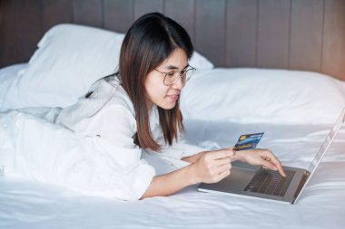 Kadın, sabah evde yatakta sipariş verirken online alışveriş için bilgisayar ve kredi kartı kullanıyor. teknoloji, ekommerce, dijital bankacılık çevrimiçi ödeme ve apartman konsepti