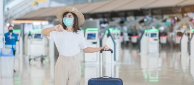 Havaalanında yürüyen yüz maskesi takan genç bir kadın, Coronavirus hastalığı enfeksiyonunu koruyan, şapkalı Asyalı bir kadın gezgin. Aşı artırıcı doz konseptinden sonra seyahat zamanı