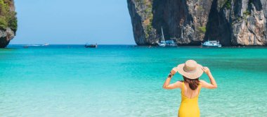 Sarı mayo ve şapkalı kadın turist, Tayland, Krabi 'deki Phi Phi Adası' ndaki Maya Körfezi plajında güneşlenen mutlu gezgin. tarihi eser, hedef Güneydoğu Asya Seyahat, tatil ve tatil konsepti