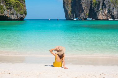 Sarı mayo ve şapkalı kadın turist, Tayland, Krabi 'deki Phi Phi Adası' ndaki Maya Körfezi plajında güneşlenen mutlu gezgin. tarihi eser, hedef Güneydoğu Asya Seyahat, tatil ve tatil konsepti