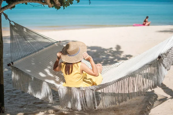 Mutlu Kadın Gezgin cennet kumsalındaki bir hamakta dinleniyor. Sarı elbiseli kadın turist tropik deniz kenarında dinleniyor. Tatil, seyahat, yaz, seyahat ve tatil konsepti.