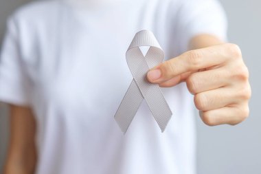 Beyin Kanseri Farkındalığı Ayı, yaşayan insanları desteklemek için gri renkli kurdele tutan kadın. Sağlık ve Dünya Kanser Günü konsepti