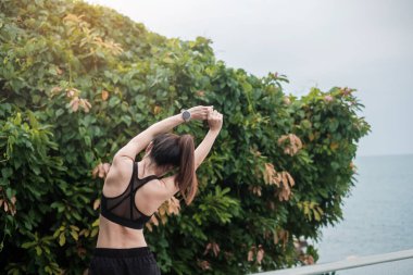 Spor kıyafetli genç bir kadın, vücudu okyanus manzarasına karşı esnetiyor, sabahları sağlıklı kadın egzersizi yapıyor. Spor, sağlık ve iş hayatı dengesi kavramları