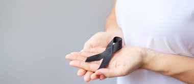 Melanoma ve cilt kanseri için siyah kurdele tutan kadın, Aşı yaralanması farkındalığı ayı, keder ve huzur içinde yatsın. Sağlık ve Irkçılık Konsepti