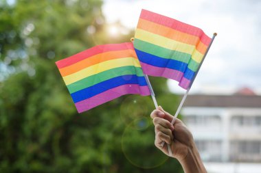 Eller yeşil doğa arka planında LGBTQ Gökkuşağı bayrağı gösteriyor. Lezbiyen, Gey, Biseksüel, Transseksüel ve Eşcinsel Topluluğuna ve Gurur Ayı kavramına destek