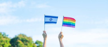 Doğa arka planında LGBTQ Gökkuşağı ve Isarael bayrağını gösteren eller. Lezbiyen, Gey, Biseksüel, Transseksüel ve Eşcinsel Topluluğuna ve Gurur Ayı kavramına destek